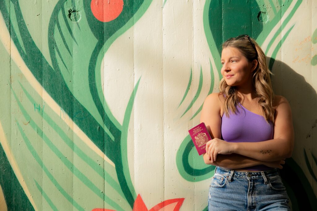 laid back travel is one of the hot blog topics for wedding businesses this year - Katherine leans against a colourful wall, passport in hand